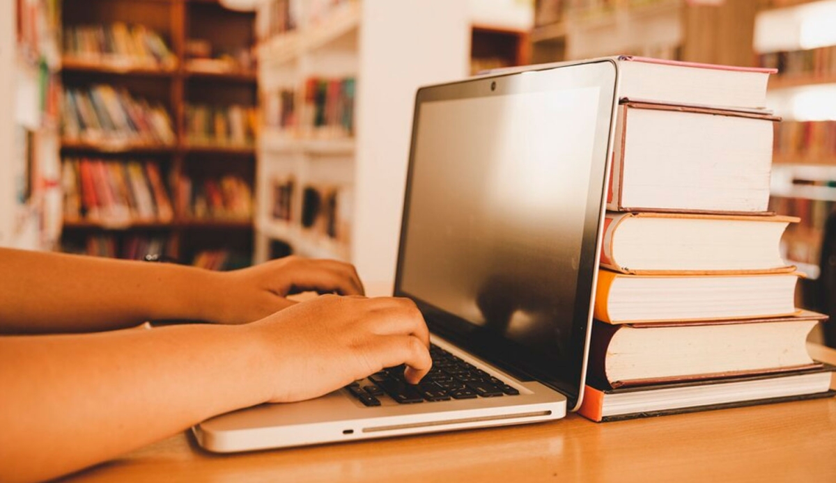 Mãos digitando sobre um computador portátil sobre uma mesa em uma biblioteca